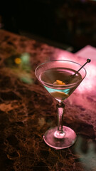 Martini cocktail glass on bar counter.  Alcoholic cocktail or non-alcoholic mocktail in pink light neon.