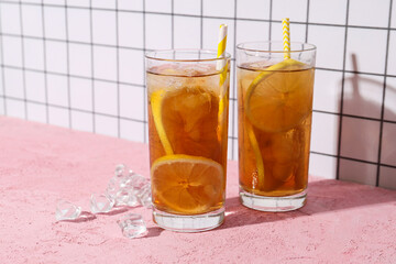 A glass of cold tea with ice and an orange on a pink background