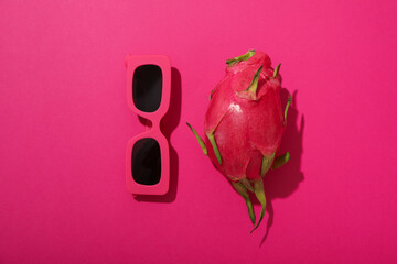 One whole dragon fruit and sunglasses on pink background, top view