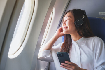 Portrait image of a woman with earphone enjoy listening to music with smart phone while traveling on an airplane