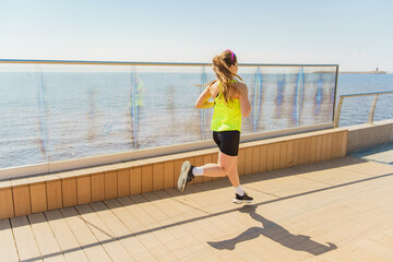 Run woman in a bright yellow tank top jogs along a waterfront boardwalk on a sunny day.