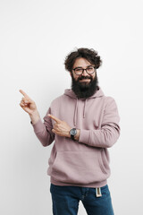 Fototapeta premium A stylish man dressed in a pink hoodie and blue jeans points emphatically to the side against a clean white background, suggesting direction, attention, or presentation.
