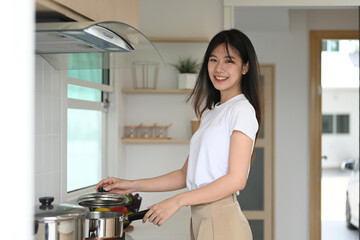 Portrait of beautiful young asian woman making a hearty soup in the kitchen and looking at camera