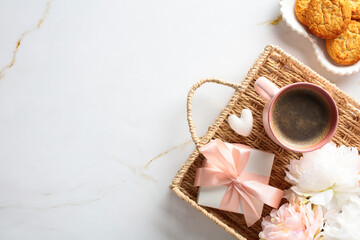 A serene coffee break setup with a cup, cookies, a gift, and flowers on a marble backdrop, perfect for lifestyle content.
