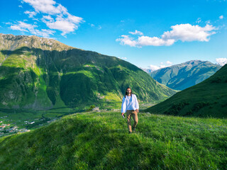 Naklejka premium long-haired man stands on the top of a green mountain in a white shirt - drone shot