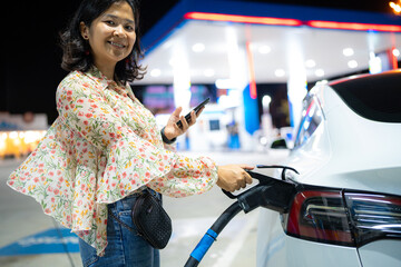 Business asian woman use smartphone waiting ev car charge station at night city