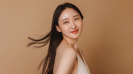 Naklejka premium Portrait of a young woman with long black hair smiling gently. Her hair flows in the wind, and she wears a beige top. 