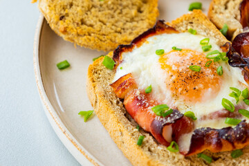 Baked Bacon and Eggs in Bread on White Plate with Fresh Green Onion Close-Up