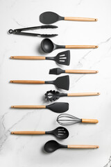 A set of kitchen utensils on a marble table. Scoop, tongs, spatula, whisk, brush
