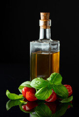 Bottle of olive oil and tomatoes with basil on a black background.