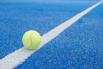 a ball on the line of a blue paddle tennis court