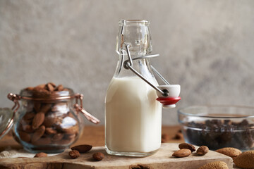 A bottle of vegan almond milk on a wooden table, with almonds and raisins in the background