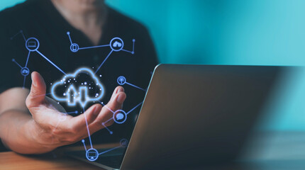 A person holding a digital cloud computing icon in front of a laptop, representing data storage and technology.