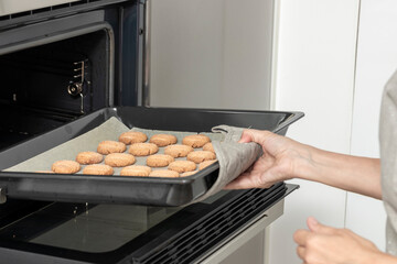 a person pulling a tray of freshly baked cookies from an oven, using a cloth for safety