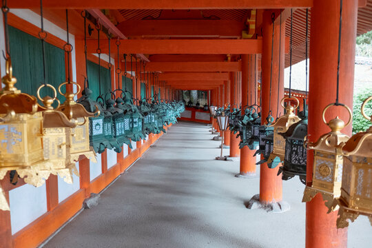 Two rows of lanterns in vibrant golden and green colors hang gracefully from a portico of a temple in Nara, Honshu