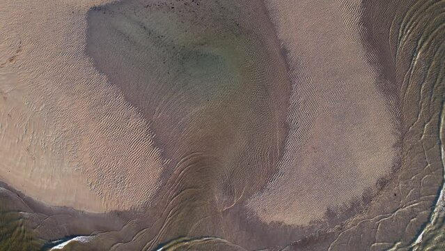 A drone view in evening sunlight, looking straight down at the sea swirling around the edge of a sand bank, in the mouth of the River Avon, Bigbury-on-Sea, south coast of Devon, southwest England, UK