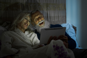 Senior couple lifestyle moments at home. Happy old man and woman watching funny stuff on a digital...