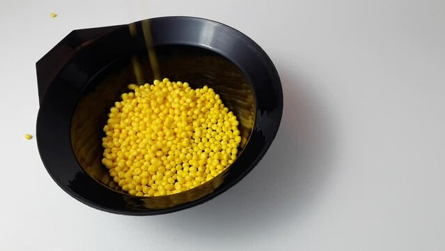 Yellow masterbatch granules fall into the black cup.Color pigment carrier polymer in the plastic industry