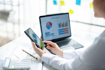 A woman is sitting at a desk with a laptop and a cell phone