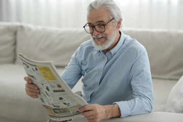 Portrait of grandpa with stylish glasses reading newspaper on sofa indoors