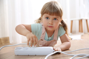 Naklejka premium Little child playing with power strip and plug on floor indoors. Dangerous situation