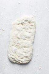 Overhead view of bread dough being shaped ion white countertop, Shaping proofed dough on a white surface, process of making artisan bread