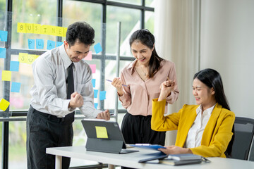 Fototapeta premium Three people are standing around a table with a laptop and a whiteboard