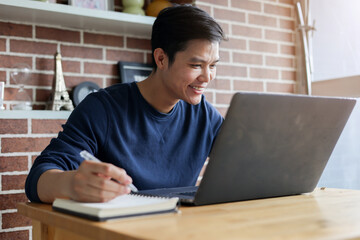 close up young asian student man sitting at the library in university and learning online course and doing assignment by writing on notebook  for education and lifestyle concept