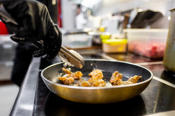A close-up of a hand using tongs to cook shrimp in a frying pan