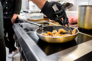 A close-up of a hand using tongs to cook shrimp in a frying pan