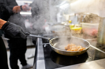 A close-up of a hand using tongs to cook shrimp in a frying pan