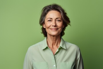 Portrait of a glad woman in her 50s wearing a simple cotton shirt isolated in pastel green...