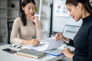 Two women are sitting at a desk, one of them is writing on a piece of paper