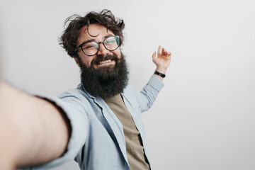A cheerful bearded man with glasses takes a selfie, exuding happiness and positivity. His joyful...