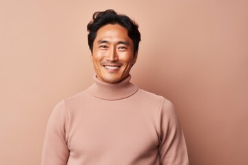 Obraz premium Portrait of a glad asian man in his 40s wearing a classic turtleneck sweater in front of pastel brown background