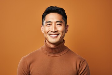 Fototapeta premium Portrait of a glad asian man in his 40s wearing a classic turtleneck sweater isolated on pastel brown background