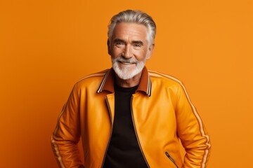Fototapeta premium Portrait of a blissful man in his 70s sporting a stylish varsity jacket while standing against soft orange background