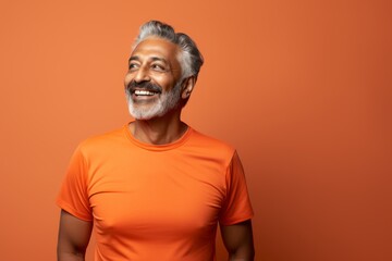 Obraz premium Portrait of a happy indian man in his 60s wearing a moisture-wicking running shirt on soft orange background