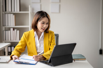 A woman in a yellow jacket is sitting at a desk with a laptop
