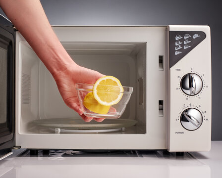 Hand holding bowl with cut lemon in front of microwave
