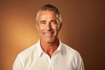 Obraz premium Portrait of a cheerful man in his 50s wearing a classic white shirt over soft brown background
