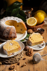 Closeup of cut bundt with pieces, lemons, nuts and green leaves, vertical, with copy space
