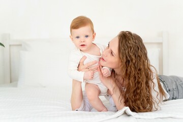 a loving mother takes care of a newborn baby, mom and baby son gently hugs and kisses at home on the bed, maternal love and care, mom plays with the baby. portrait of a happy mother with a child,