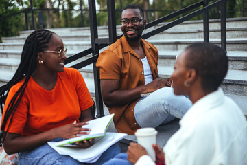 Two women and one man, all African-American university students, converse and share notes while...