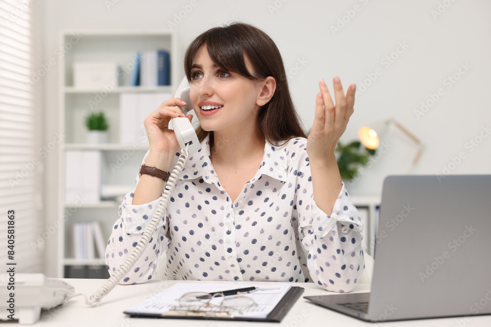 Sticker Smiling secretary talking on telephone at table in office