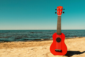 A red ukulele lies on sandy beach under sunny weather