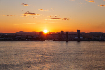 Obraz premium Sunset behind the Quebec City port installations in silhouette, with the St. Lawrence River in the foreground, Quebec, Canada