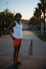 Hip young Brazilian male model showcasing swimwear, sunglasses and summer fashion while posing in front of palm trees