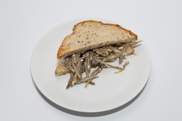 Dried anchovy sandwich on a white plate isolated against a white background.