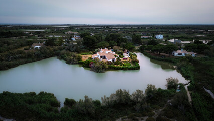 Fototapeta premium Aerial top view of a typical house in the Camargue swamps where we can see pine trees of the region, water and a white house with red tiles 